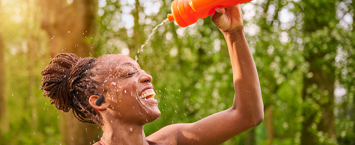 Femme se rafra&icirc;chissant en versant de l&rsquo;eau sur sa t&ecirc;te tout en portant des &eacute;couteurs de sport Philips en ext&eacute;rieur